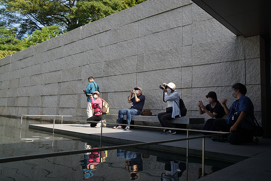 晴れた空の下で、鈴木大拙館の「水鏡の庭」を撮影する人々の様子